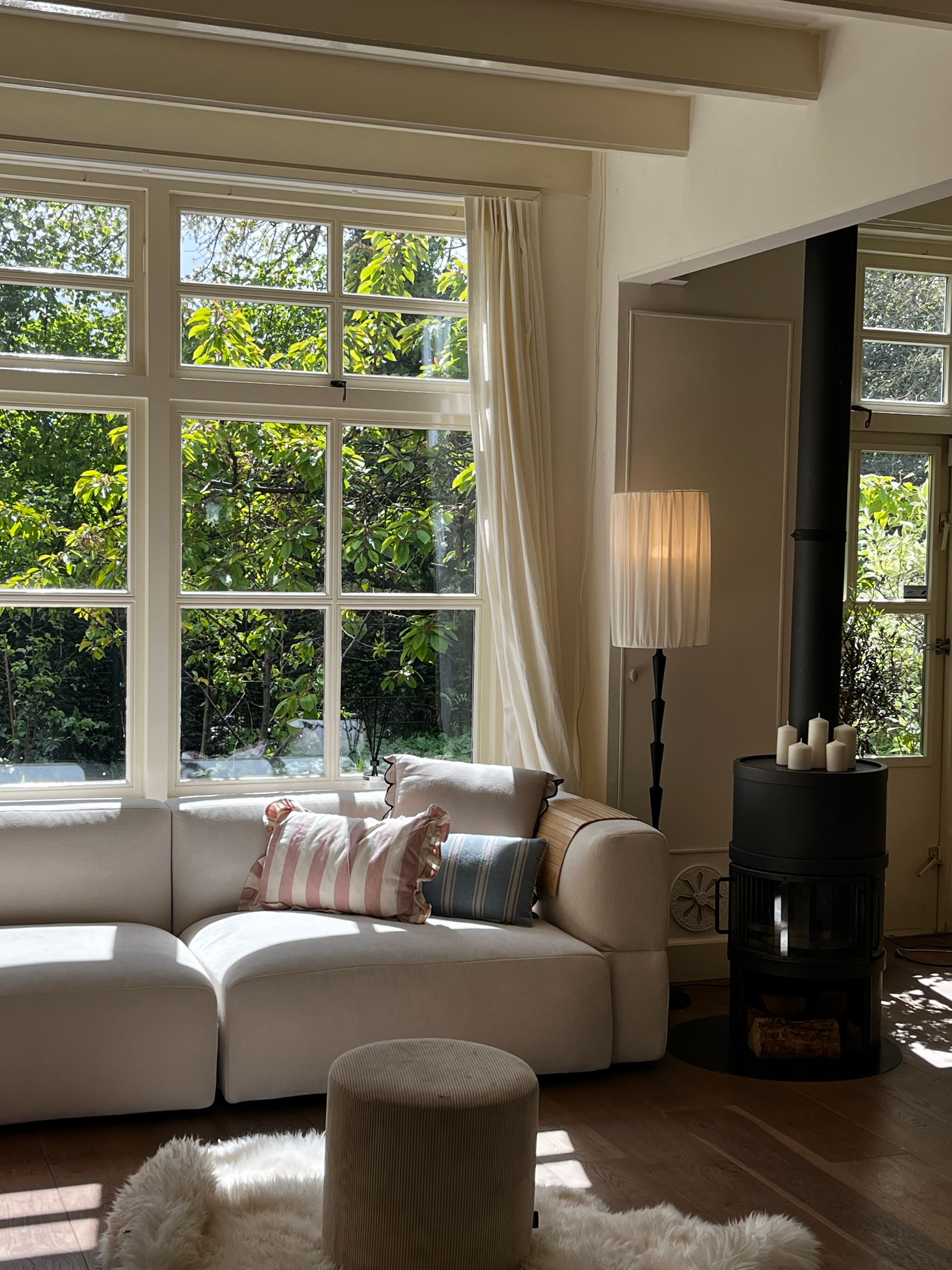Sunlit West Michigan VRBO living room with wood stove, cream sofa, and forest views